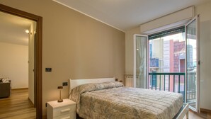 A bedroom with a bed, bedside tables, a nightstand, a window with a view of buildings, and a door. - Lovely apartment in Recco with WiFi (Recco)
