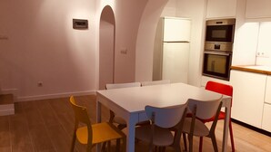 Ein Essbereich mit weißem Tisch und vier Stühlen, eine Küche mit weißen Schränken und Geräten sowie ein Holzboden.