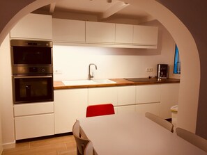 A modern kitchen with white cabinetry, stainless steel appliances, a wooden countertop, and a red chair. - Marina house with private mooring & large terrace - Port Canigó (Roses)