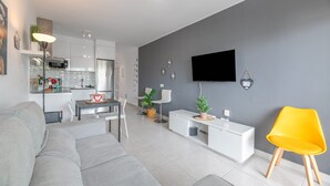 A modern living room with a grey sofa, a dining table, a white TV stand, and a bright yellow chair. - Vacation Apartment 'Casa Amor Costa Teguise' with Wi-Fi (Costa Teguise)