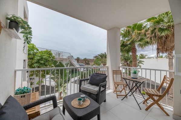 A balcony with wicker furniture, a table with a mug, and potted plants.