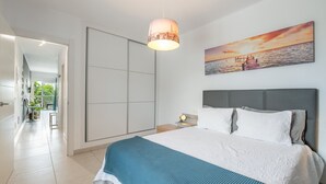 A modern bedroom with a large bed, a nightstand, a wall-mounted lamp, and a painting of a sunset over water. - Vacation Apartment 'Casa Amor Costa Teguise' with Wi-Fi (Costa Teguise)