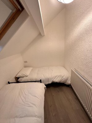Um quarto pequeno e estreito com duas camas, um radiador e teto inclinado.