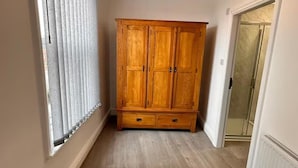 Een gang met een houten garderobe, een raam met zonwering en een deur naar een andere kamer.