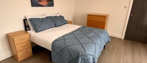 A bedroom with a bed, a nightstand, a dresser, a door, and a painting on the wall.