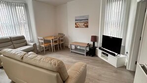 Een woonkamer met een bank, een televisie, een tafel en stoelen.