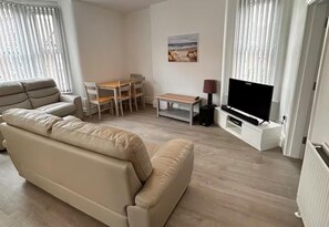 Ein Wohnzimmer mit einer Couch, einem Fernseher, einem Tisch und Stühlen.