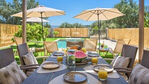 Zona pranzo all'aperto con vista piscina, arredamento in vimini e ombrelloni.