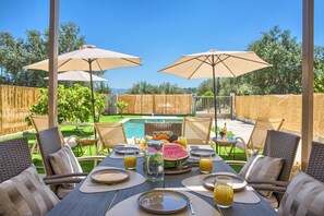 An outdoor dining area with a pool view, wicker furniture, and umbrellas. - Villa Charaki VPR, Villa (Rhodes)