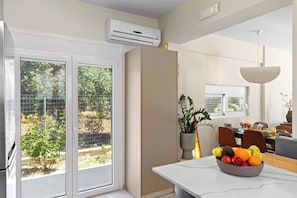 A modern kitchen with a large window, an air conditioning unit, and a dining area with a fruit bowl. - Villa Charaki VPR, Villa (Rhodes)