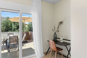 Una habitación moderna con puerta de vidrio que da a un área de estar exterior, una mesa pequeña con una silla y un jarrón con ramas secas.