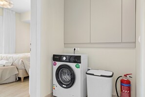Una lavadora y secadora compactas en una habitación con una cama y un extintor.