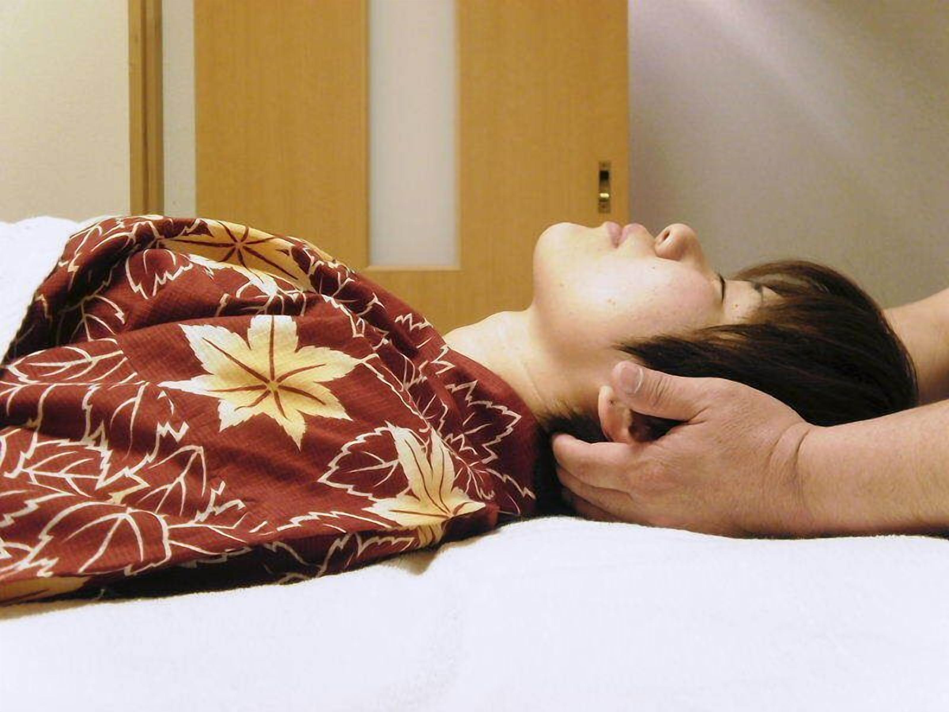 A person lying on a bed with a patterned blanket.