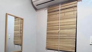 A room with a wall-mounted air conditioner, a mirror, a window with bamboo blinds, and a potted plant. - Family-Friendly Room in Siargao Air-Conditioned (General Luna)