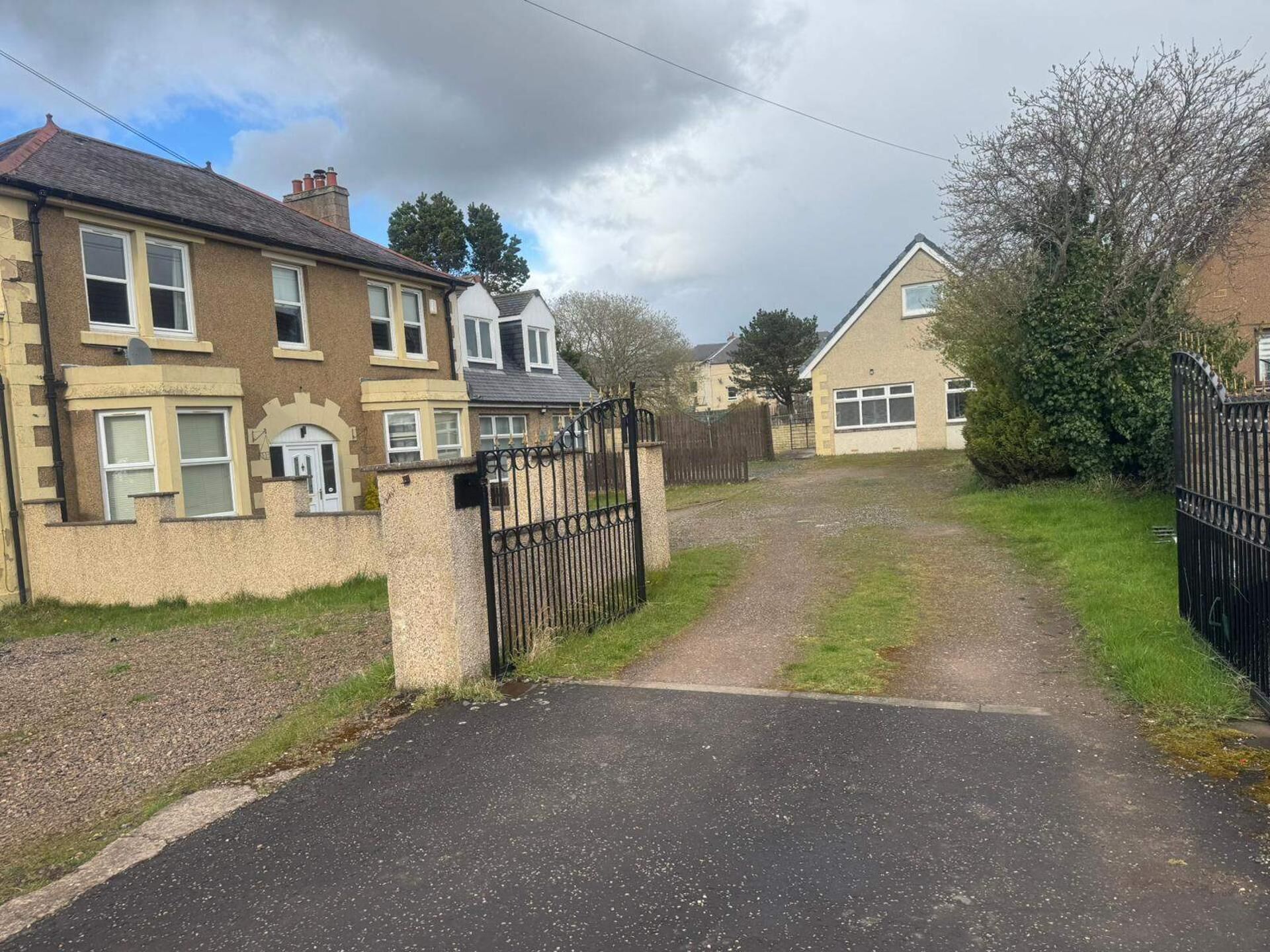 A residential street with houses, a gated driveway, and a clear sky.