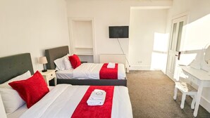 Hotellihuone, jossa on kaksi sänkyä, televisio, peilillä varustettu työpöytä ja patteri.