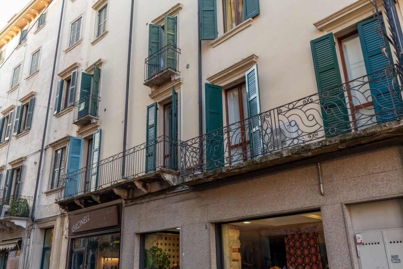 Un bâtiment doté de nombreuses fenêtres, dont certaines sont équipées de volets, et d’un balcon orné de balustrades en métal ouvragé.
