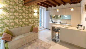 Une cuisine chaleureuse avec un plafond en bois, un papier peint à motifs floraux, un canapé blanc agrémenté de coussins et un petit îlot central avec des tabourets de bar.