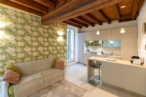 A cozy kitchen with a wooden ceiling, a floral wallpaper, a white sofa with cushions, and a small island with bar stools. - New Bridge House - Domus Verona (Verona)
