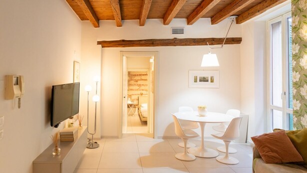 Una sala de estar moderna con una televisión de pantalla plana, una mesa de comedor con sillas, un sofá y un amplio ventanal con cortinas.