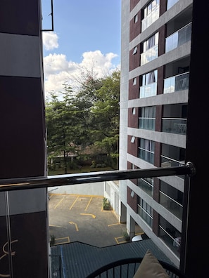A view from a balcony overlooking a parking area with a building in the background. - Tranquil 1-bedroom Apartment in Lavington, Nairobi (Nairobi)