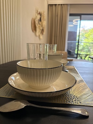 A dining table with a white bowl and matching plate, a knife, and a decorative wall piece. - Tranquil 1-bedroom Apartment in Lavington, Nairobi (Nairobi)