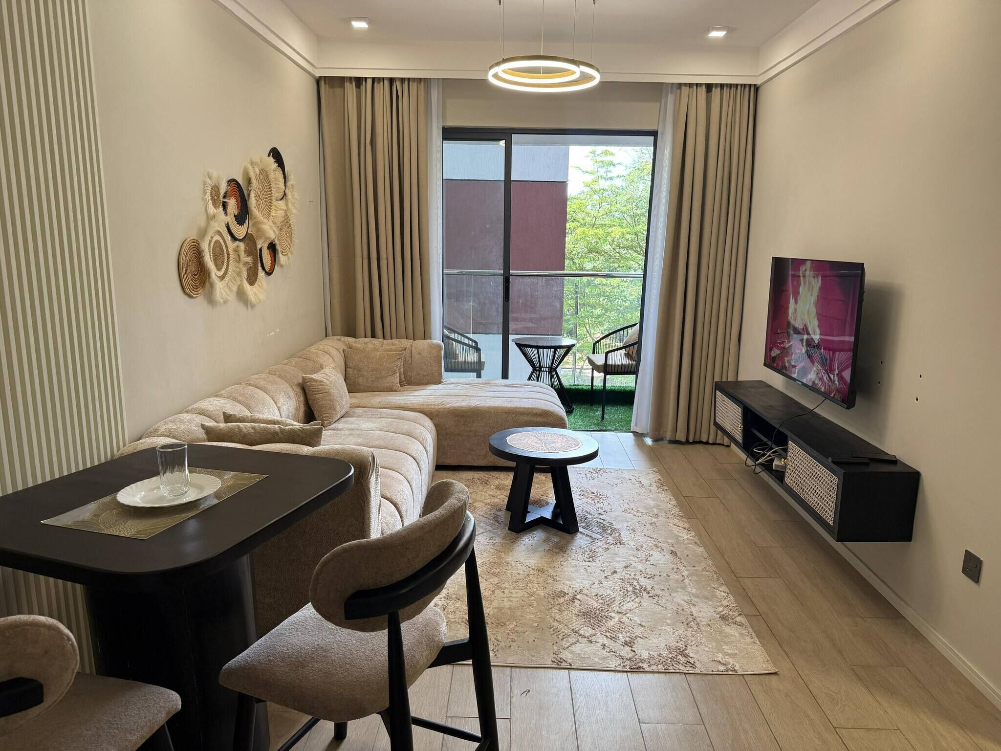 Een moderne woonkamer met een hoekbank, een eettafel met stoelen, een televisie en een balkon met uitzicht.