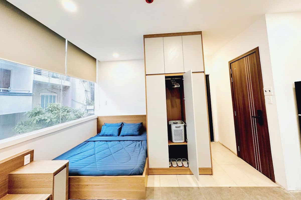Un dormitorio con cama, armario, mesita, ventana y puerta.
