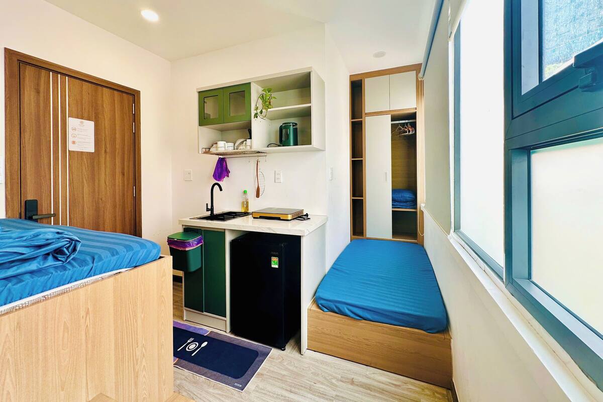 Habitación compacta con dos camas, kitchenette, baño pequeño y armario con ventana.