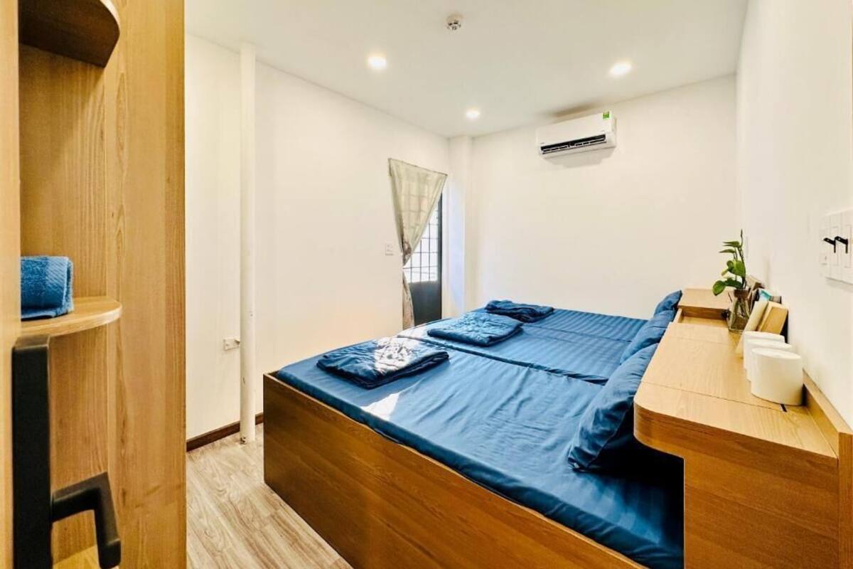Un dormitorio con cama, escritorio de madera, unidad de aire acondicionado y ventana con cortinas.