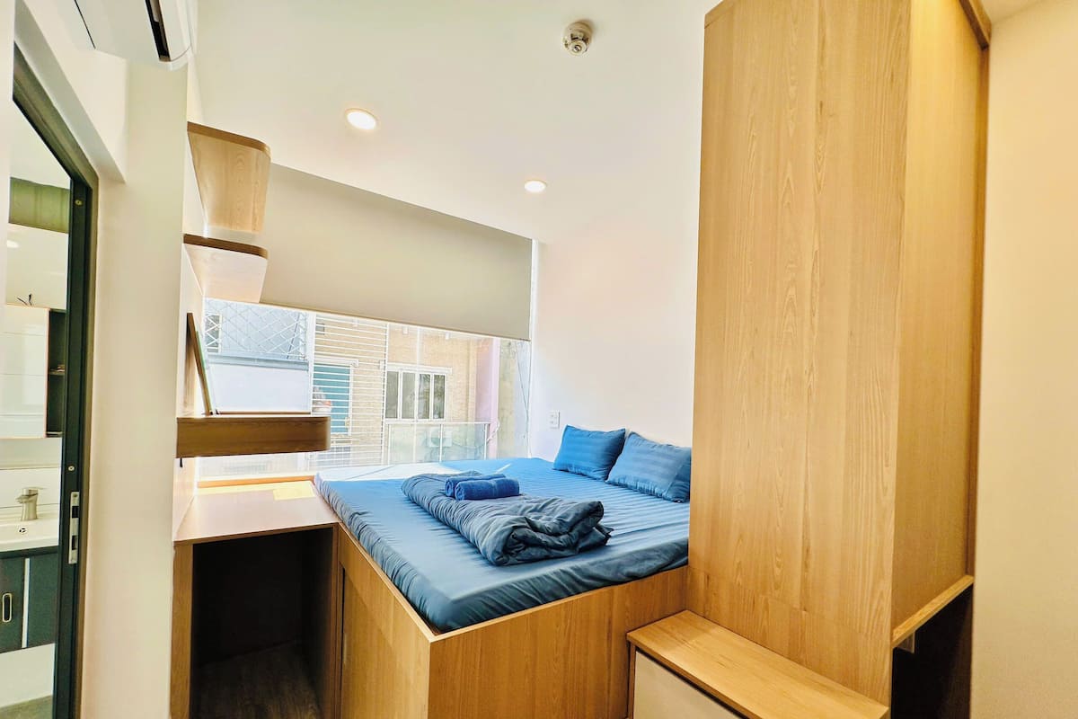 Una habitación compacta con cama, escritorio integrado y ventana con vistas a un edificio.