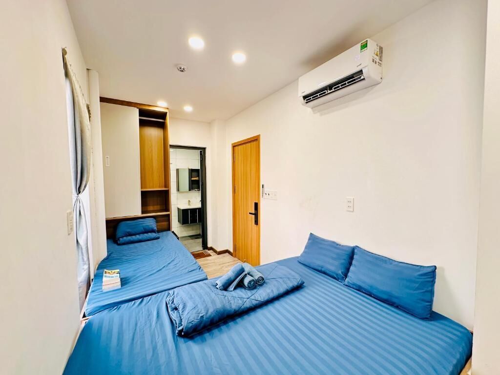 Ein Zimmer mit zwei Betten, einer Holztür, einer Klimaanlage und einer kleinen Küchenzeile.