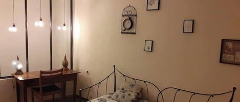 A bedroom with a bed, a desk, and a chair. There are wall-mounted lights and framed pictures.