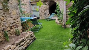 Un muro de piedra, una pequeña piscina y dos sillas verdes en un jardín.