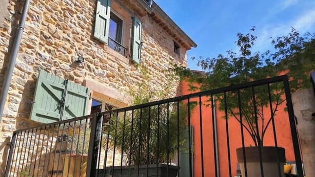 Un edificio de piedra con una valla de metal, una planta en maceta y un muro rojo.