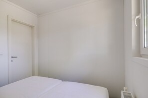 A white room with a bed, a door, and a window. - Cube 11 | Cabin in the Fruits | Zennewijnen, Betuwe (Zennewijnen)