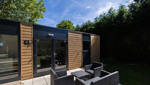 Un área de estar moderna al aire libre con puerta de vidrio, placa de número y un patio con mobiliario de mimbre.