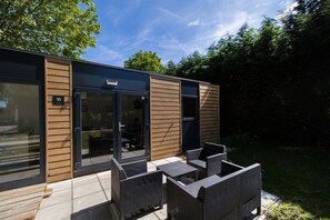 A modern outdoor seating area with a glass door entrance, a number plaque, and a patio with wicker furniture.