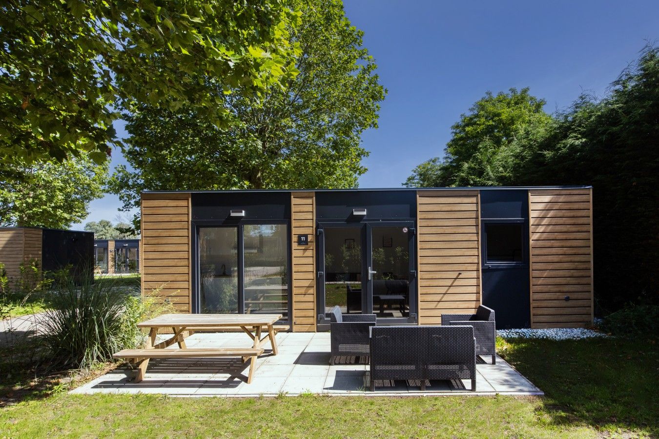 A modern outdoor seating area with a wooden table and chairs, a glass door entrance, and a number '11' sign.