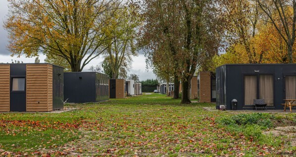 A row of modern, compact cabins with a grassy lawn and trees in the background.