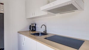 Una cocina moderna con un lavamanos de acero inoxidable, una cafetera y un armario blanco.