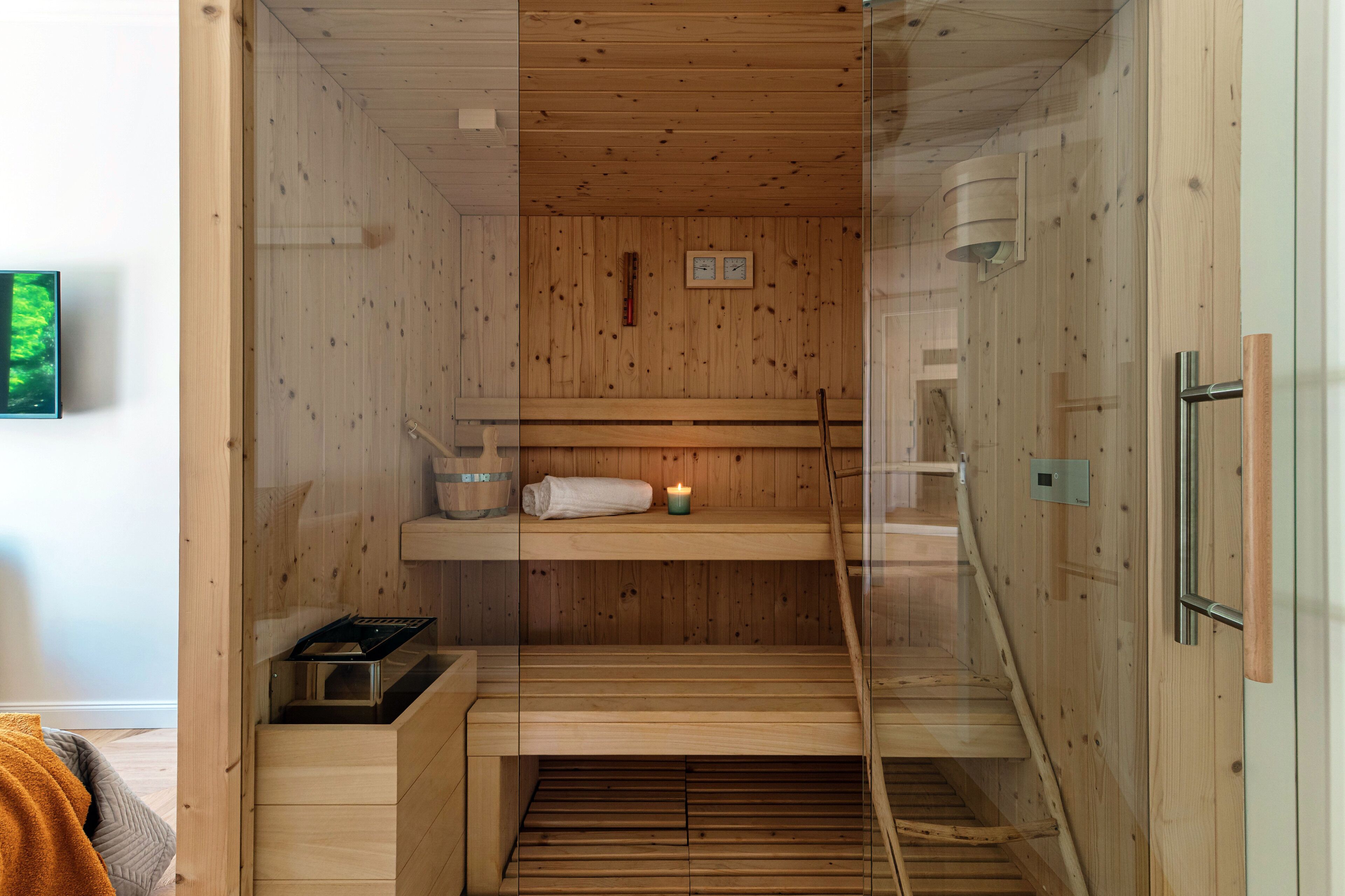 Una sauna con pareti in legno, una panca, un asciugamano, una candela e un piccolo ripiano.