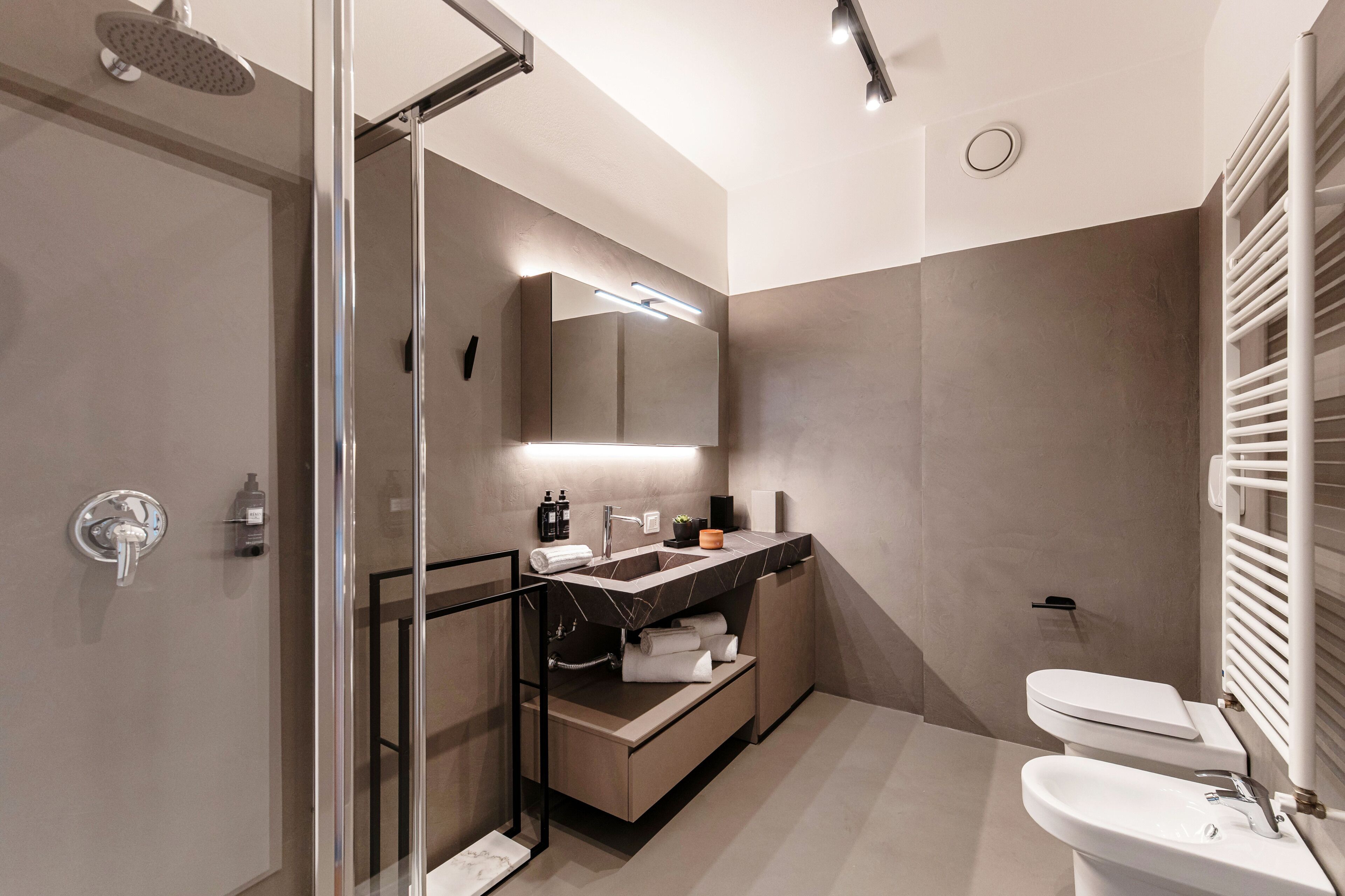 Un baño moderno con ducha de vidrio, tocador con espejo y retrete.