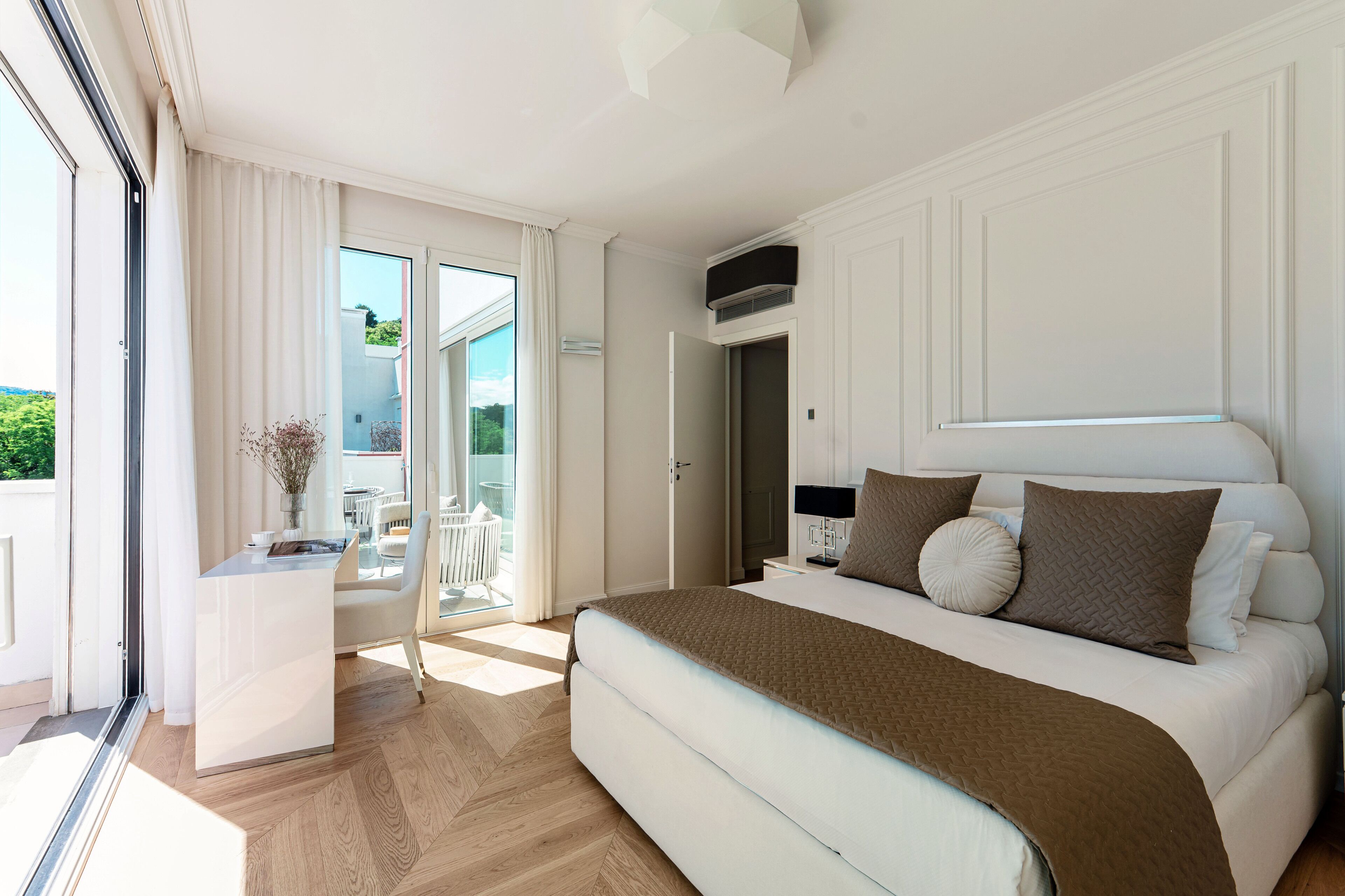 A bedroom with a large bed, a small desk, and a sliding glass door leading to a balcony.
