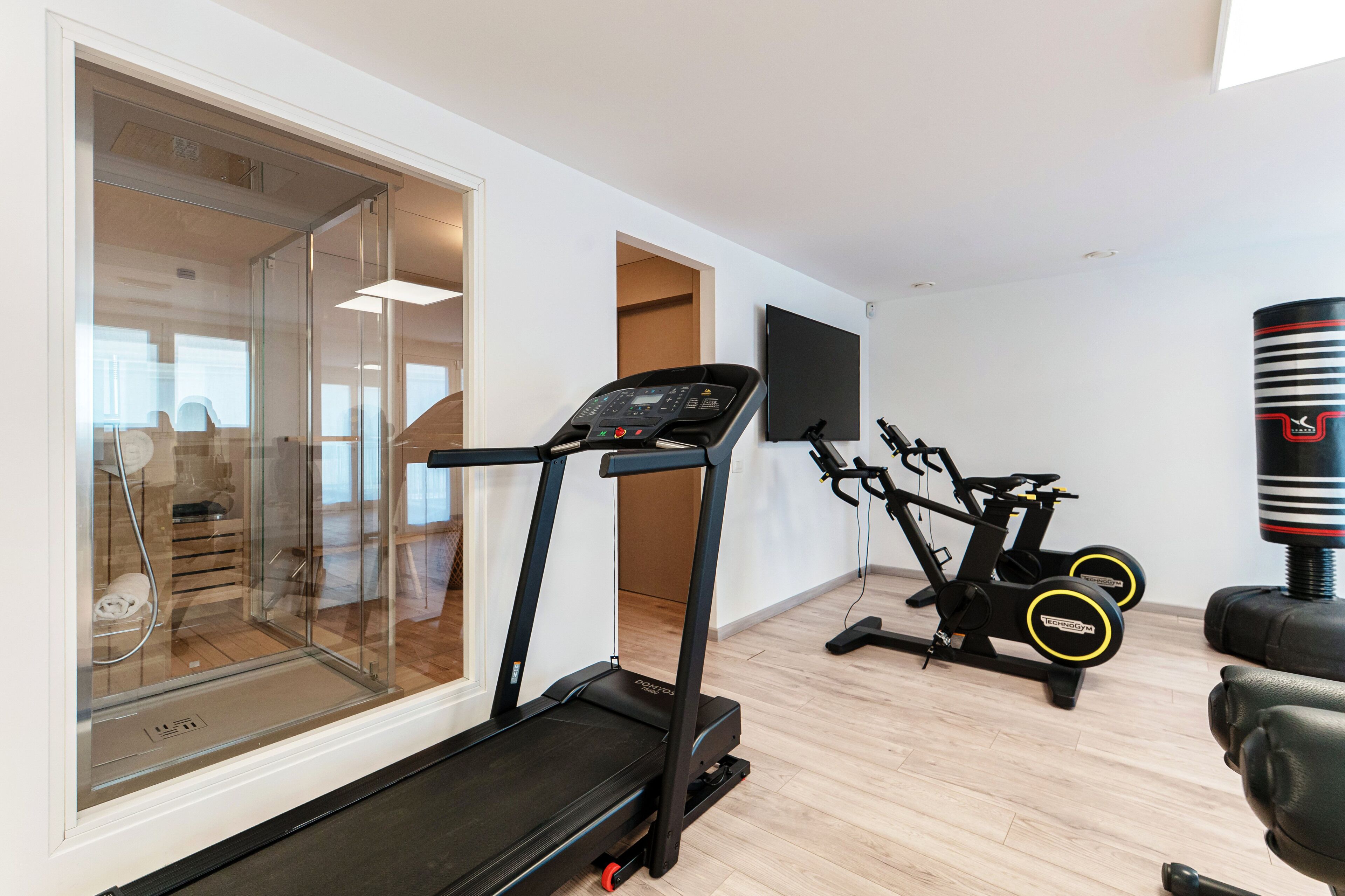 A home gym with a treadmill, stationary bike, punching bag, and a glass door leading to a shower area.