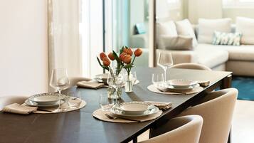A dining table set with plates, glasses, and a vase of flowers, with a sofa and a view of a pool in the background.