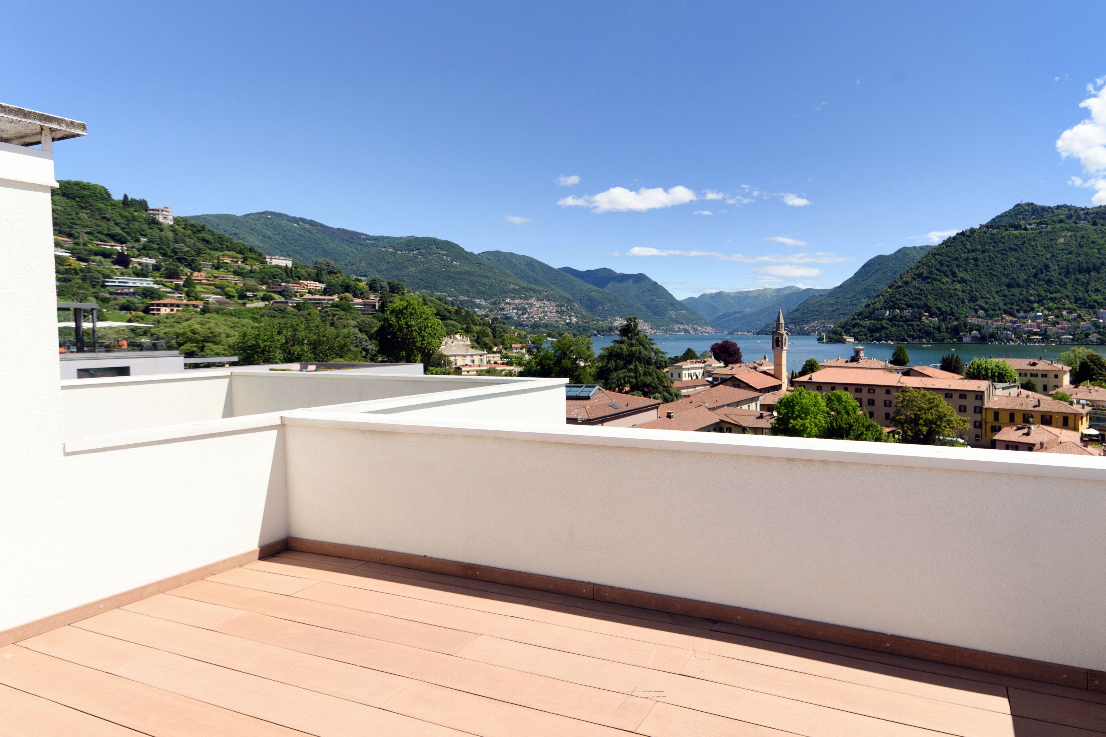 A terrace with a view of a lake and mountains, a white building, and a clock tower.