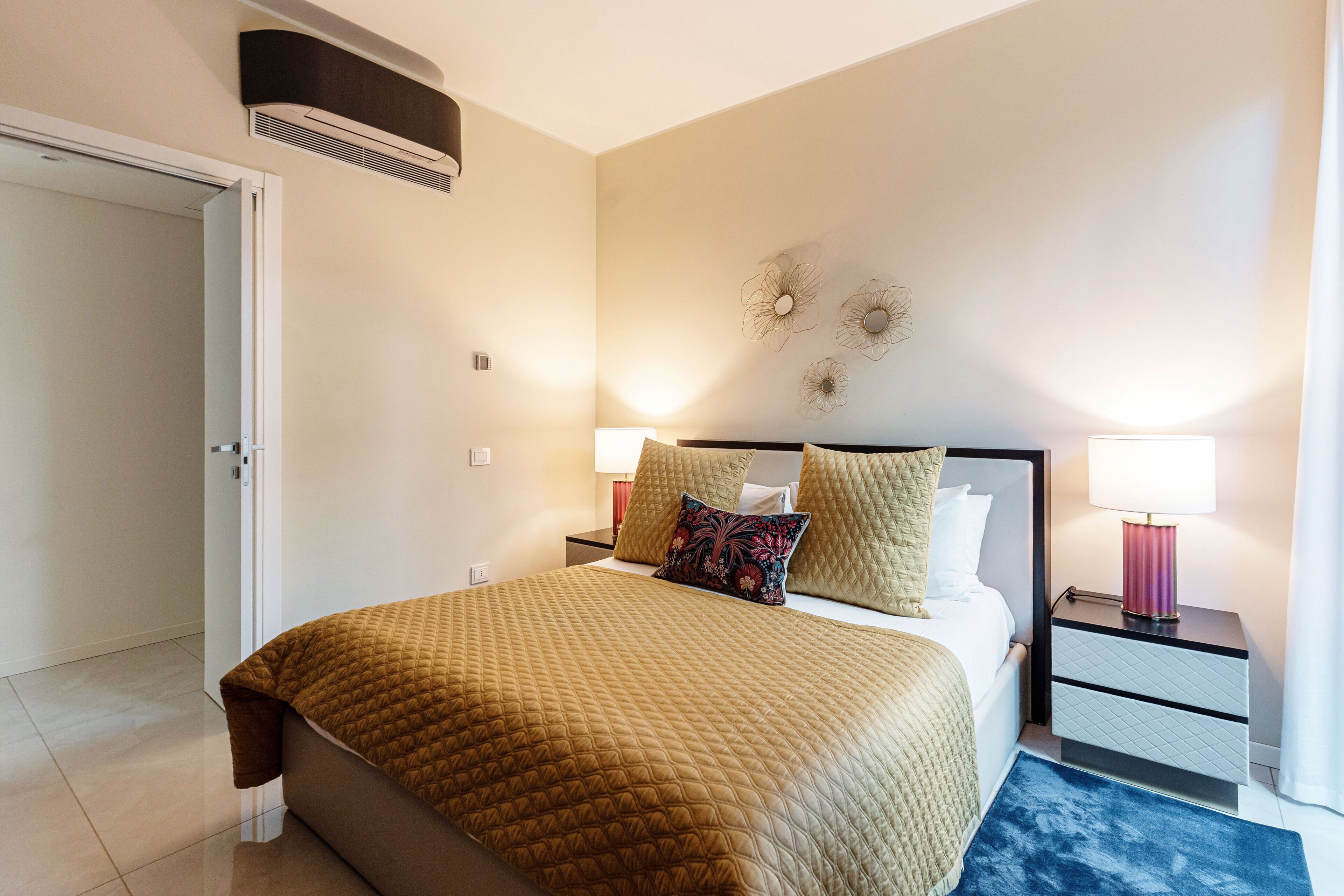 Een slaapkamer met een bed, nachtkastjes, lampen en een deur.