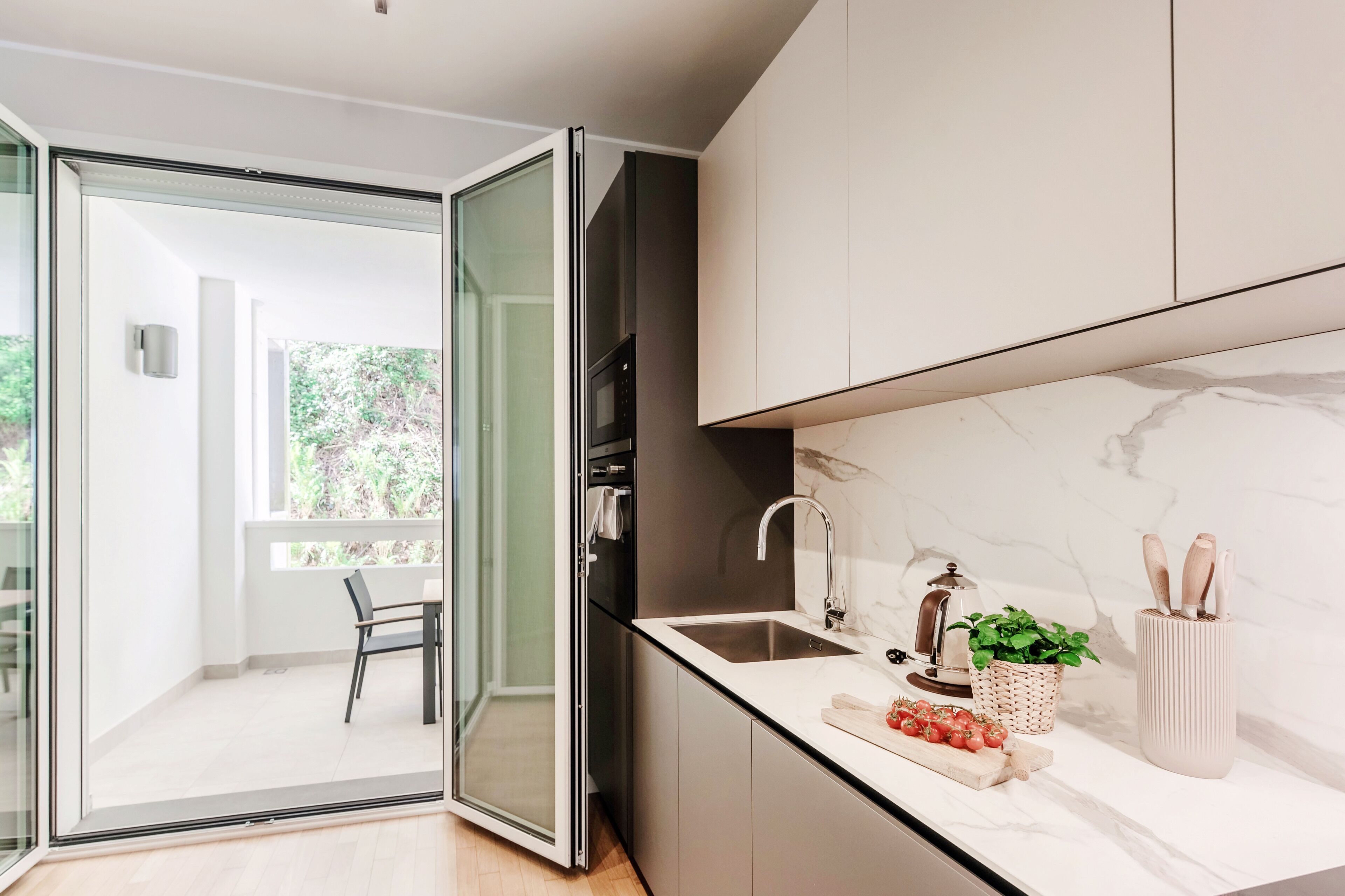 Una cocina moderna con puerta de vidrio que da a un balcón, un lavamanos y una encimera con una planta y utensilios.