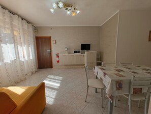 A room with a dining table, chairs, a sofa, a TV, and a fire extinguisher. - Familiar Base for a Comfortable Stay in Rosolina (Rosolina)